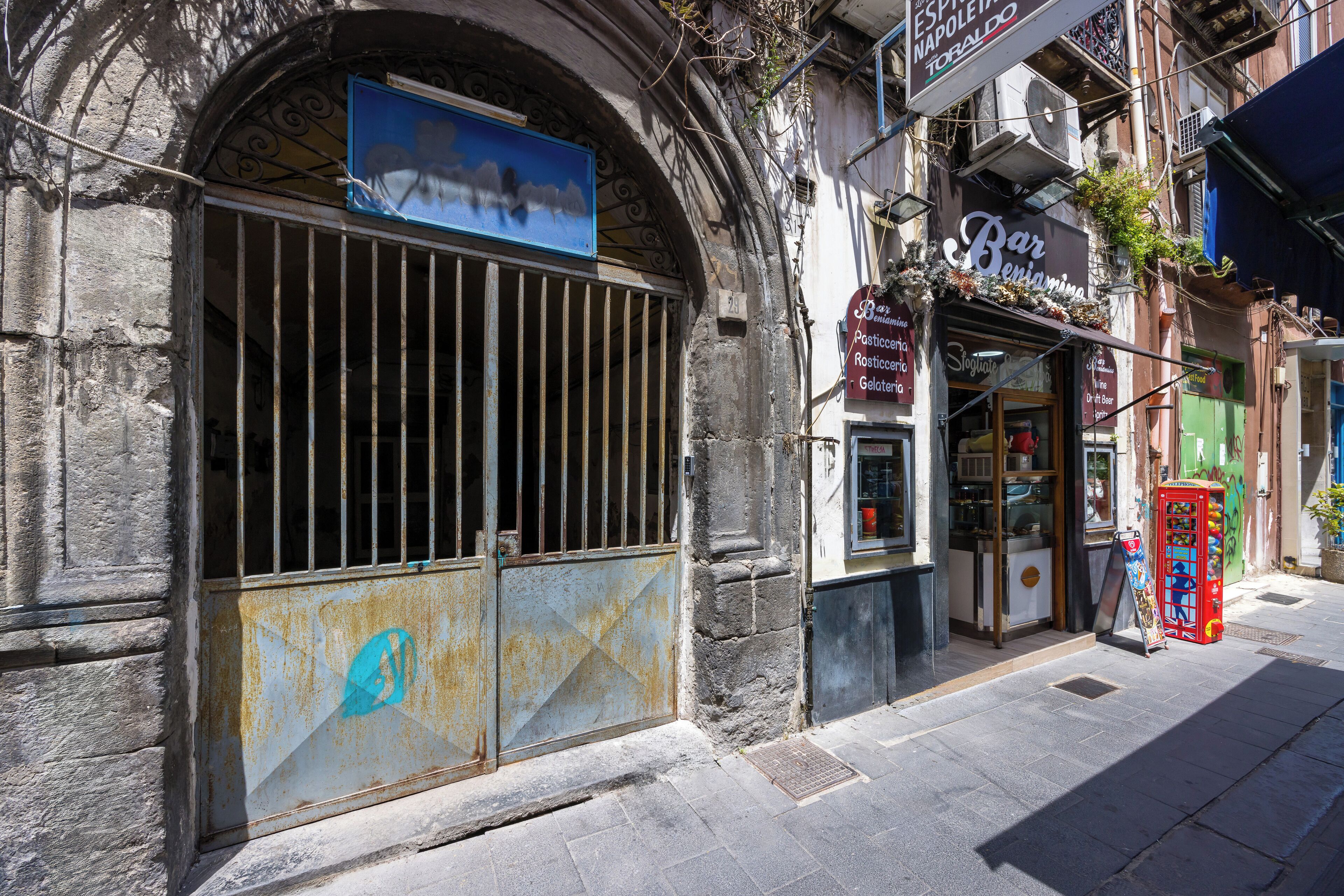 Un bar llamado Bar Benjamina con una fachada rústica, una entrada visible y una máquina expendedora roja en la acera.