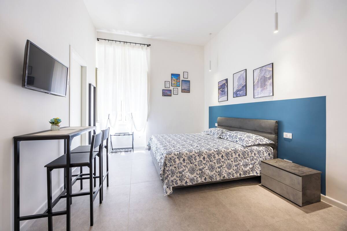 A bedroom with a bed, bedside table, and a desk with chairs.