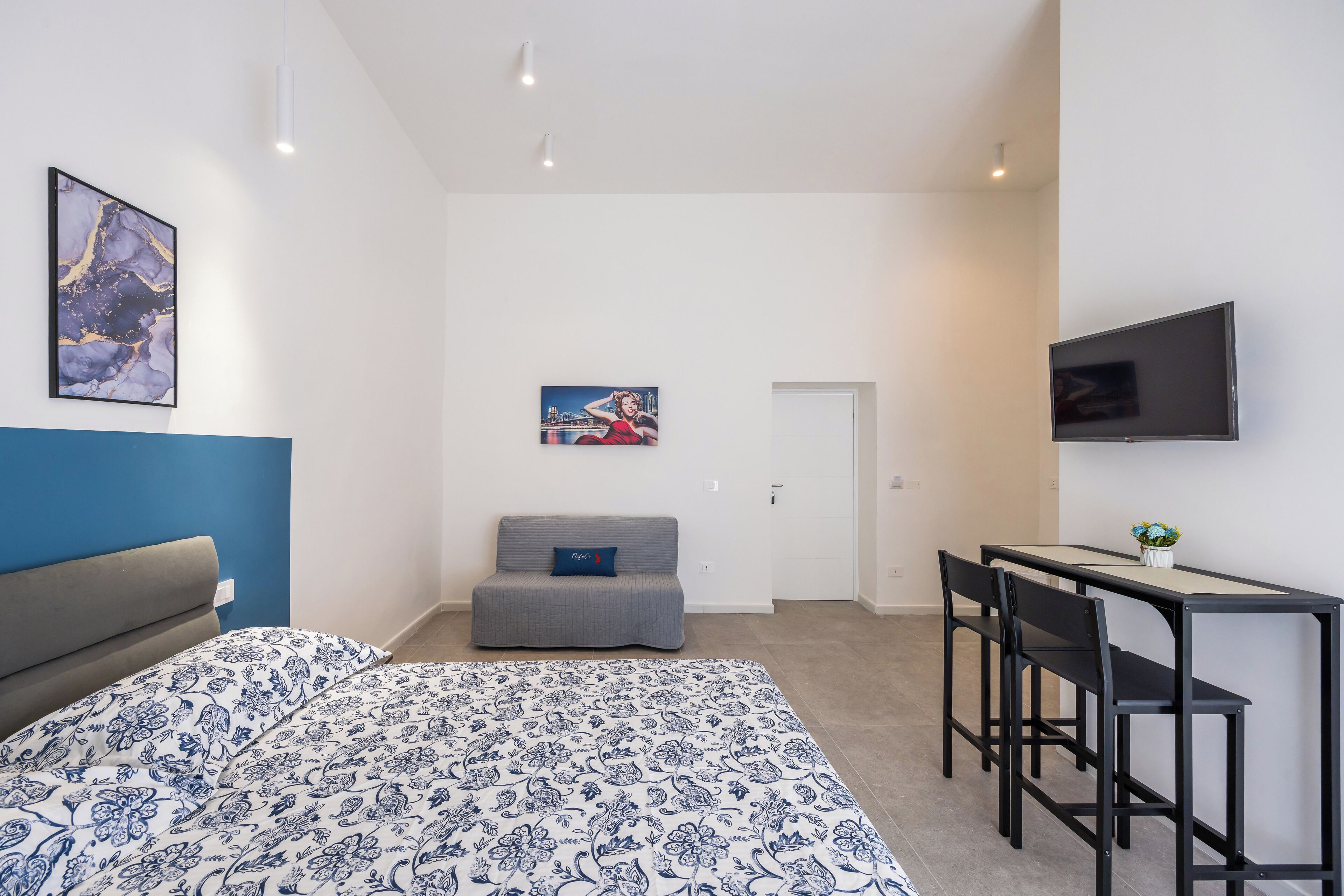 A modern bedroom with a bed, a desk with two chairs, a television, and artwork on the walls.