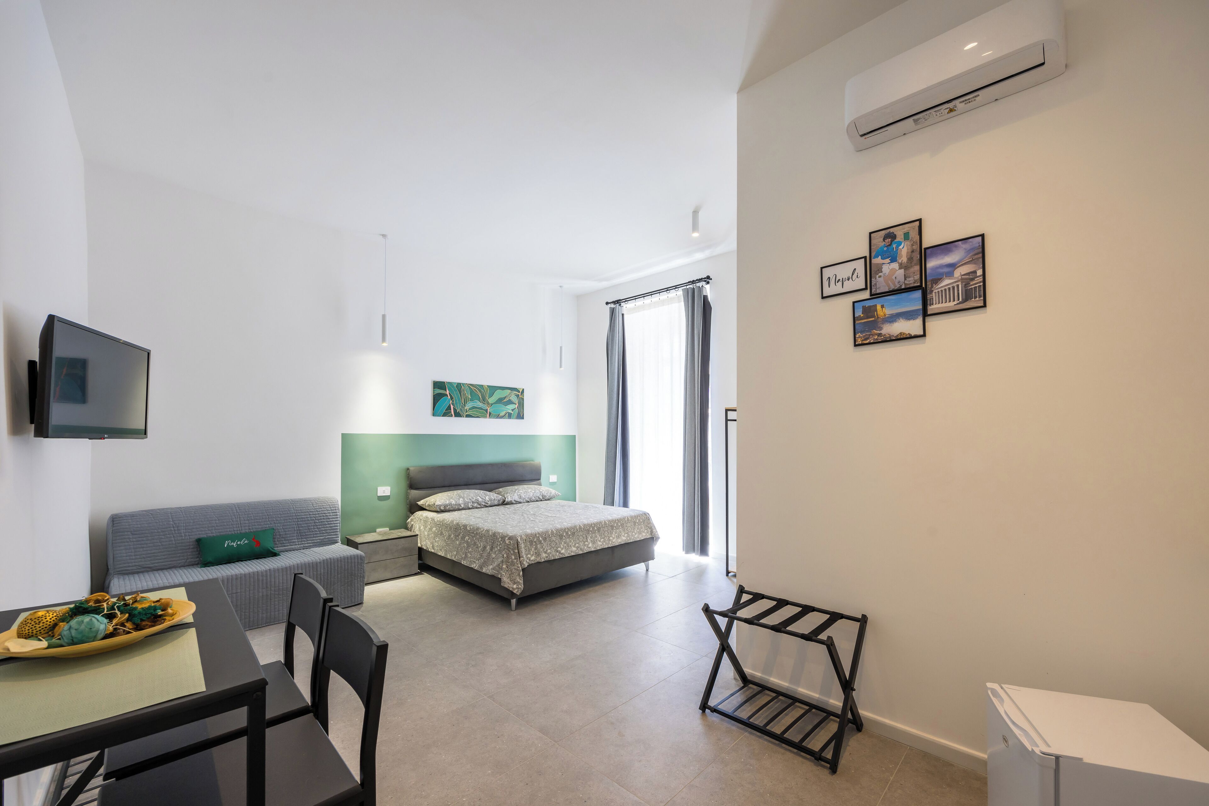 A modern hotel room with a bed, a desk, a chair, a TV, and a small table with a tray.