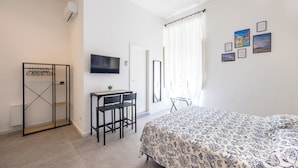 A bedroom with a bed, a desk with chairs, a TV, and a wardrobe. - Nefelu apartments (Naples)