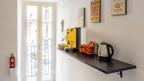 A hallway with a black shelf holding a yellow kettle, orange baskets, and framed pictures on the wall. - Nefelu apartments (Naples)