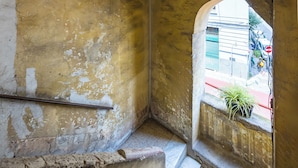 A narrow, arched passageway with rough, weathered walls and a small window with a plant. - Nefelu apartments (Naples)