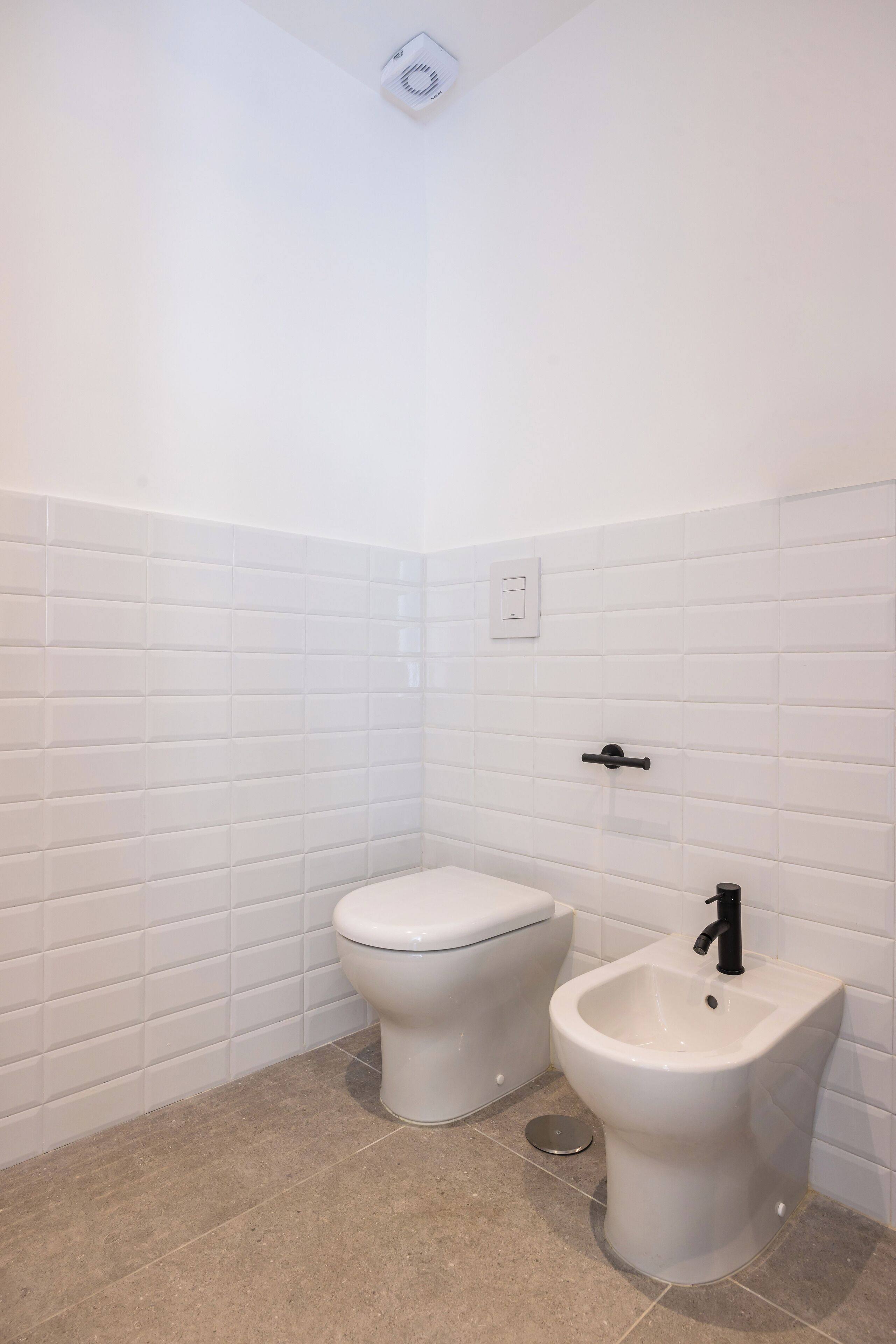 A bathroom with white tiled walls, a toilet, and a bidet.