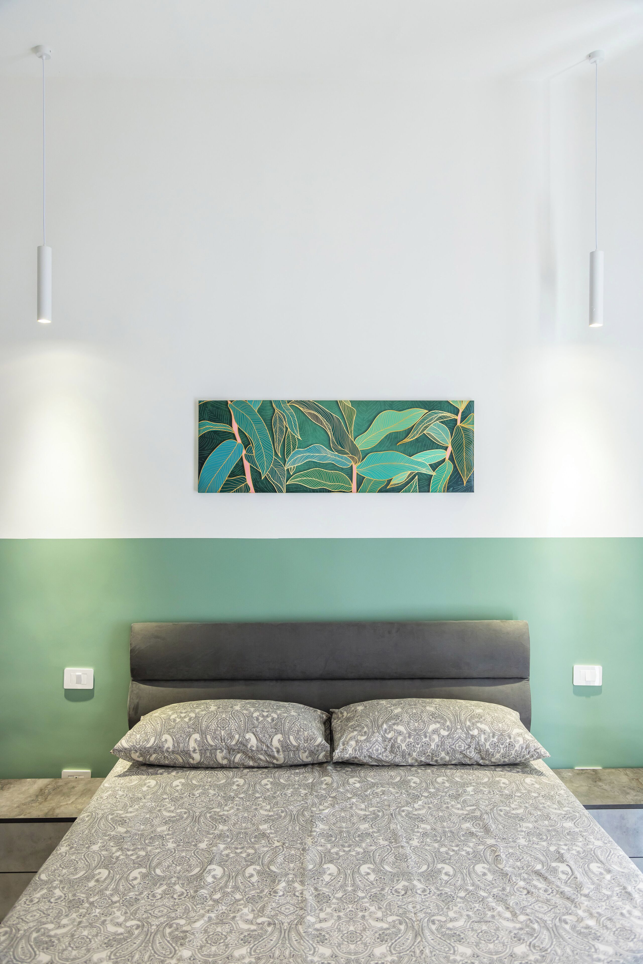 Un dormitorio con una cama, una pared verde y un cuadro de hojas.