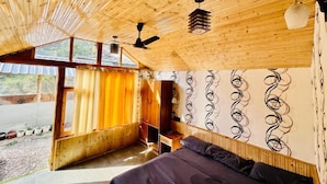 A bedroom with a wooden ceiling, a bed, a ceiling fan, and a window with curtains. - The Aisling House (Bhuntar)