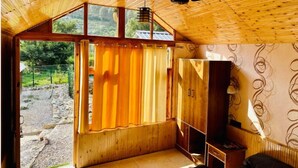 A room with a wooden ceiling, a ceiling fan, a window with curtains, and a wardrobe. - The Aisling House (Bhuntar)