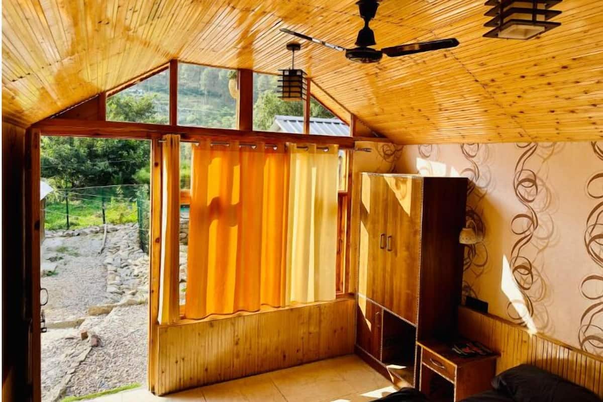 A room with a wooden ceiling, a ceiling fan, a window with curtains, and a wardrobe.