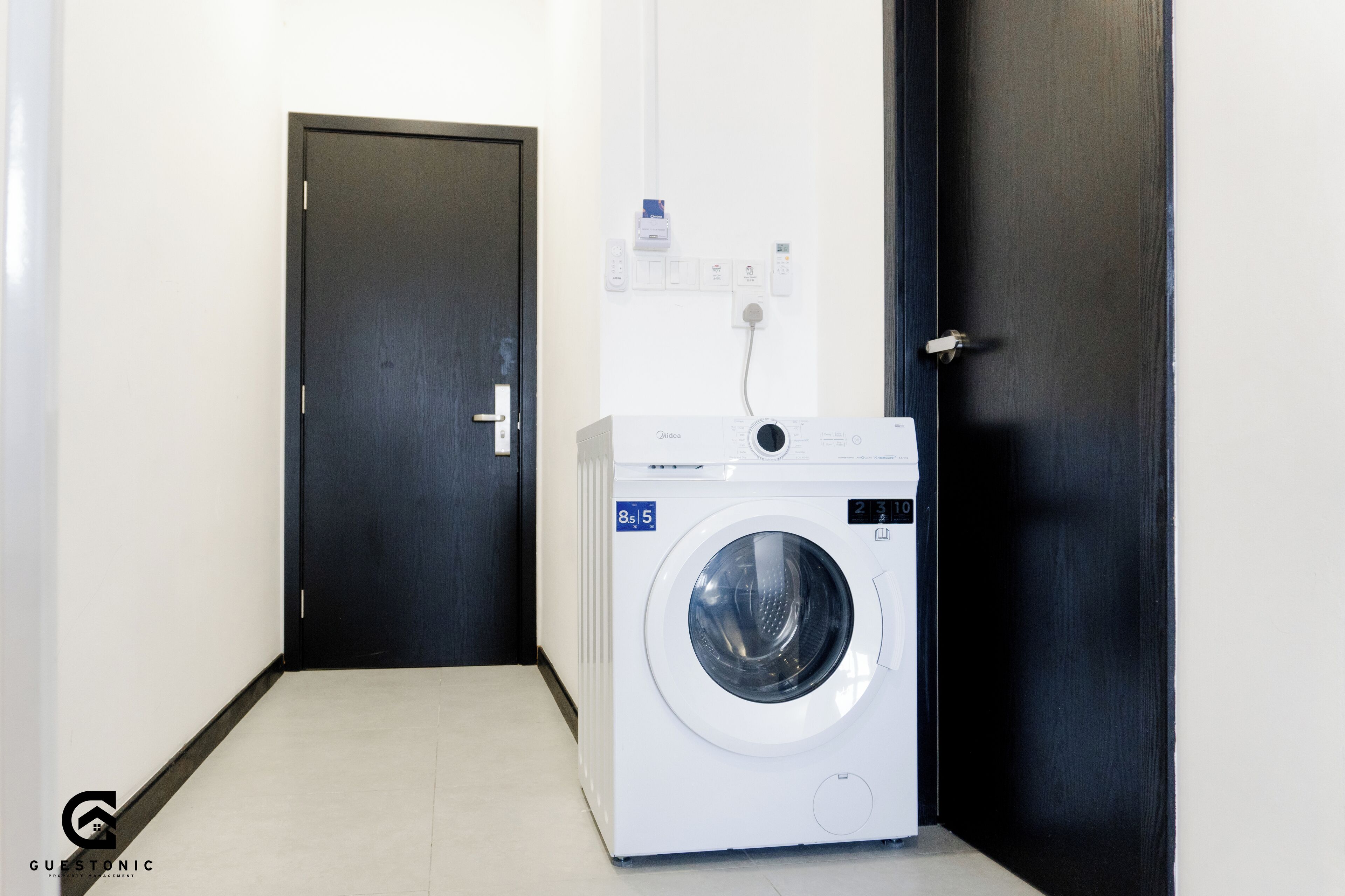A laundry room with a white washing machine, a door, and a wall-mounted electrical outlet.