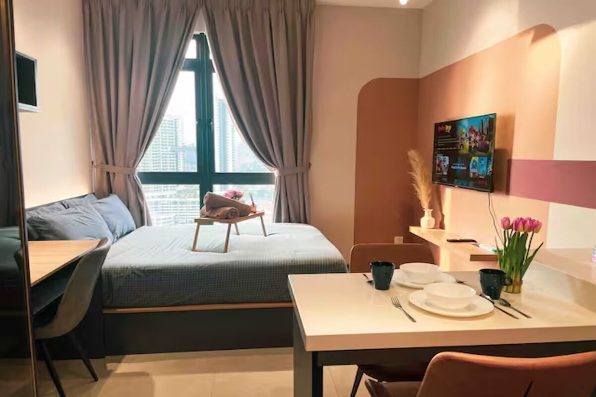 A modern hotel room with a bed, a dining table set for two, a small table with a tray, and a window with curtains.