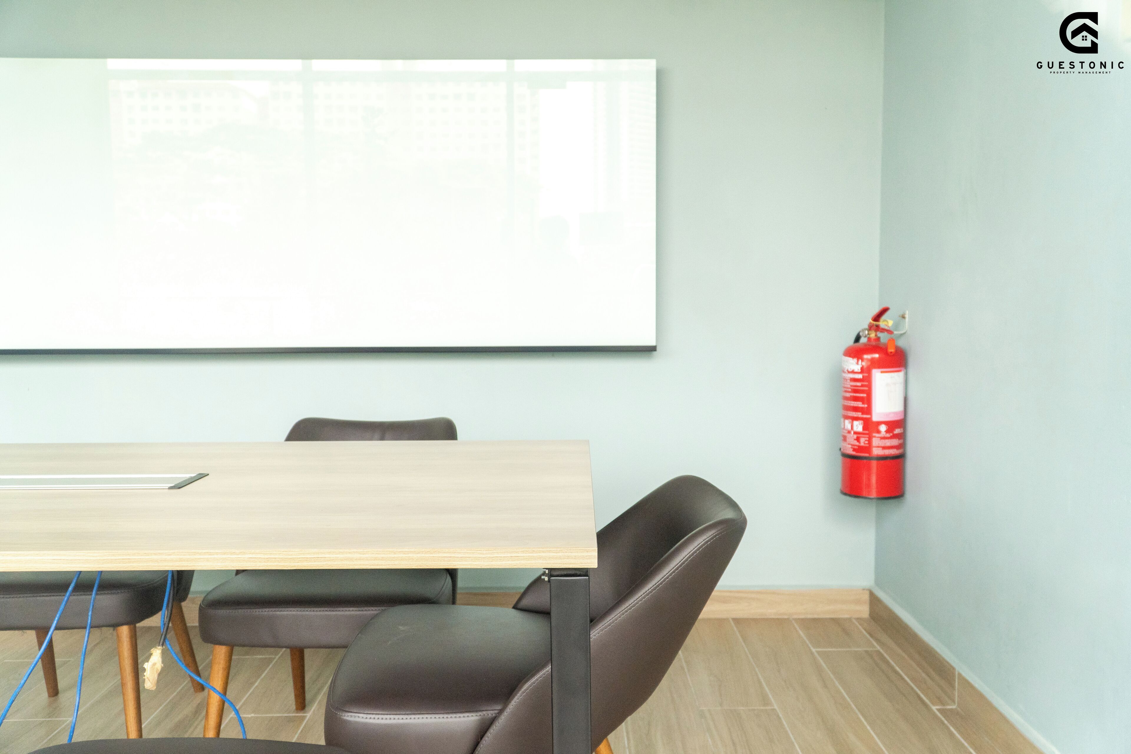 A conference room with a wooden table, black leather chairs, a whiteboard, and a red fire extinguisher on the wall.