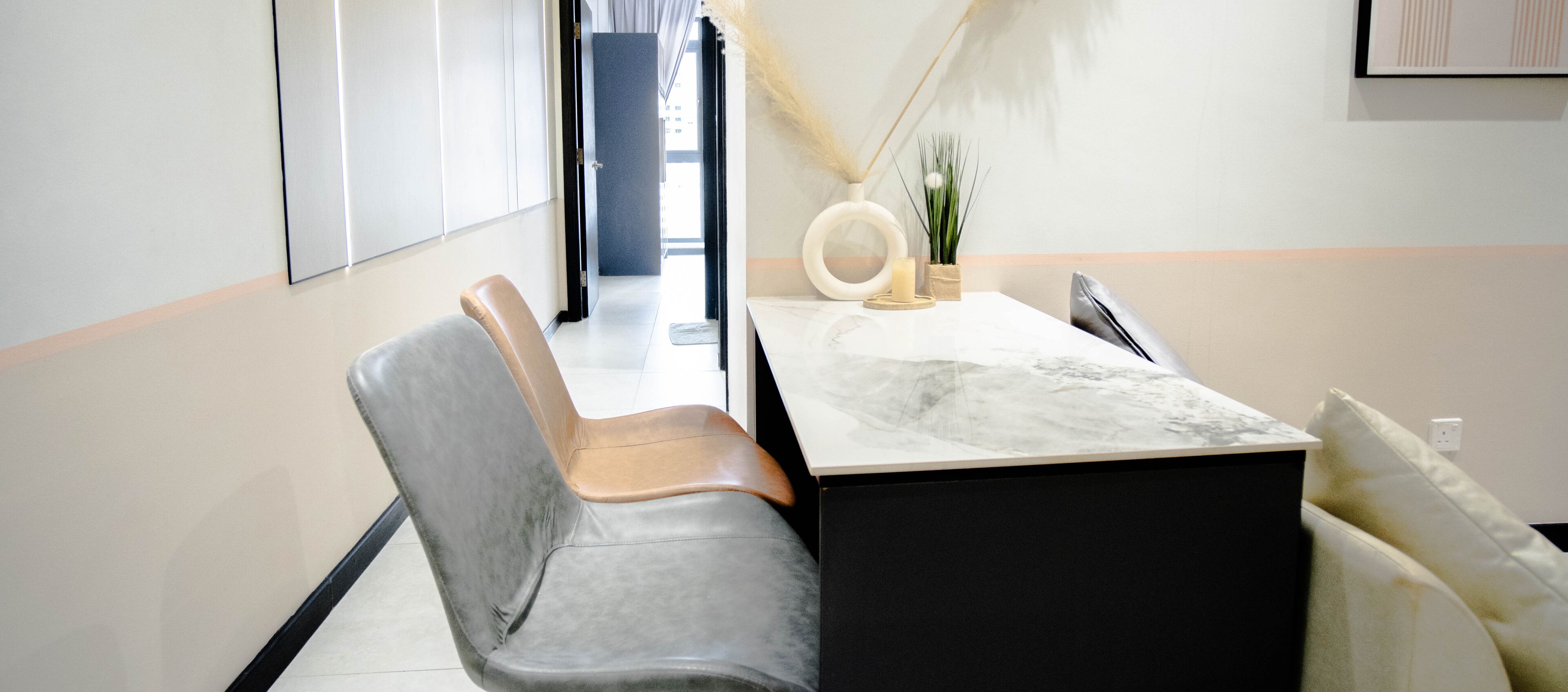 A modern hotel room with a marble-top desk, leather chairs, a small side table with a candle, and a decorative plant.