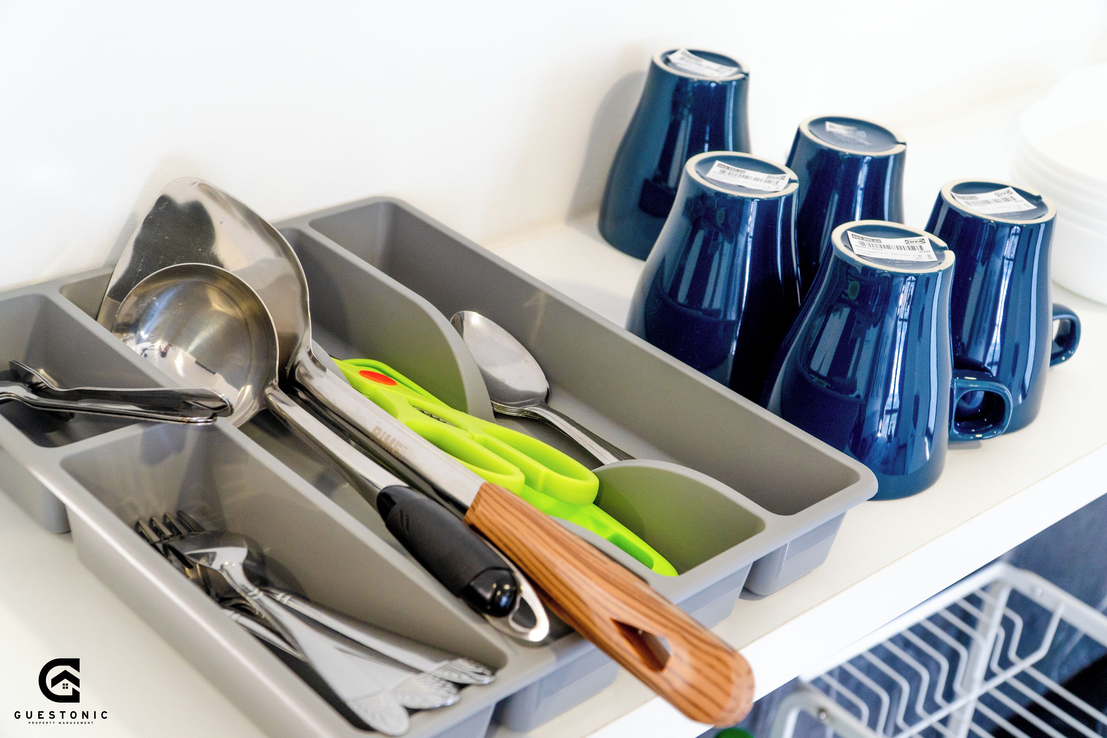 Un cajón de cocina con utensilios, un cuchillo de mango verde y tazas azules.