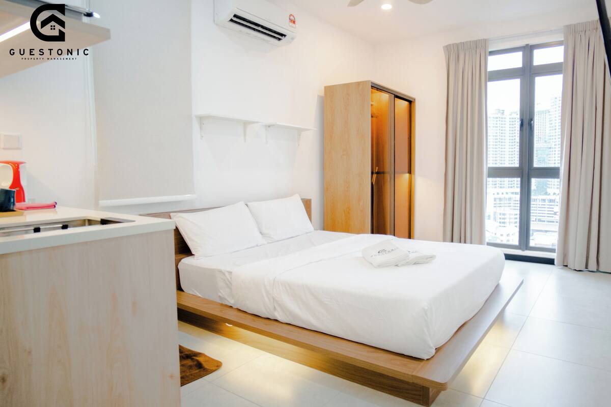 A modern hotel room with a bed, a wardrobe, a desk, and a window with curtains.