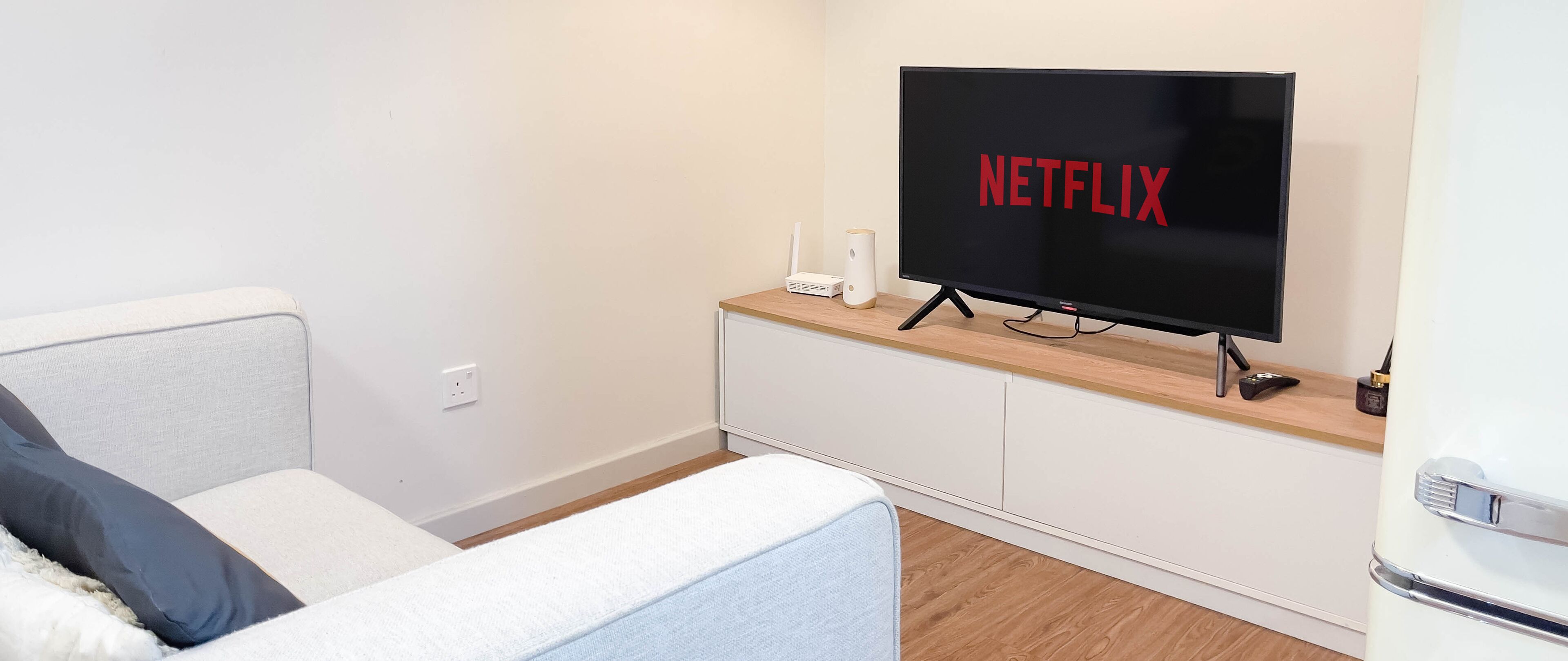 Moderni olohuone, jossa on seinälle asennettu taulutelevisio, puinen tv-taso, harmaa sohva ja valkoinen kaappi.