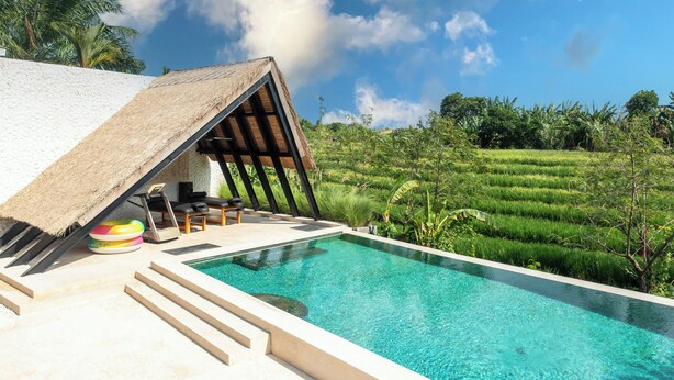 A poolside area with a thatched-roof structure, a pool, and lush green fields in the background. - Villa Kubu Dewi Sri by Villa Finder (Canggu)