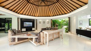 A modern living room with a curved ceiling, a flat-screen TV, a sofa, a coffee table, and a console table. - Villa Kubu Dewi Sri by Villa Finder (Canggu)
