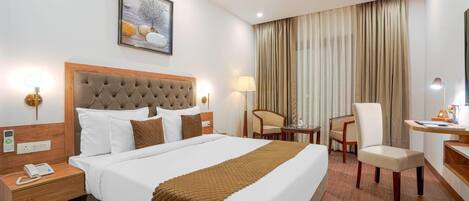 A hotel room with a large bed, a desk, a chair, a ceiling fan, and a painting on the wall.