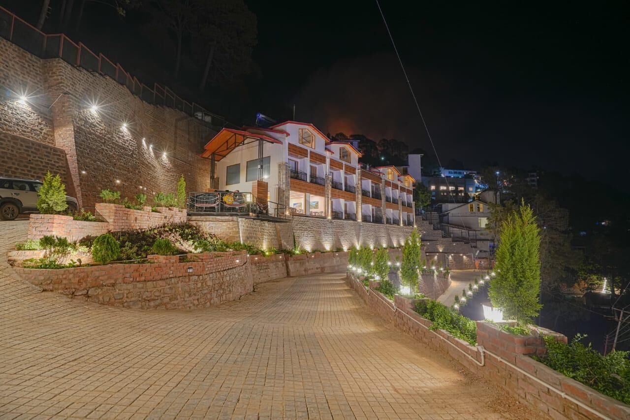 A hotel with a modern design, featuring a multi-story structure with a red and white color scheme, located on a hillside with a paved pathway leading to the entrance.