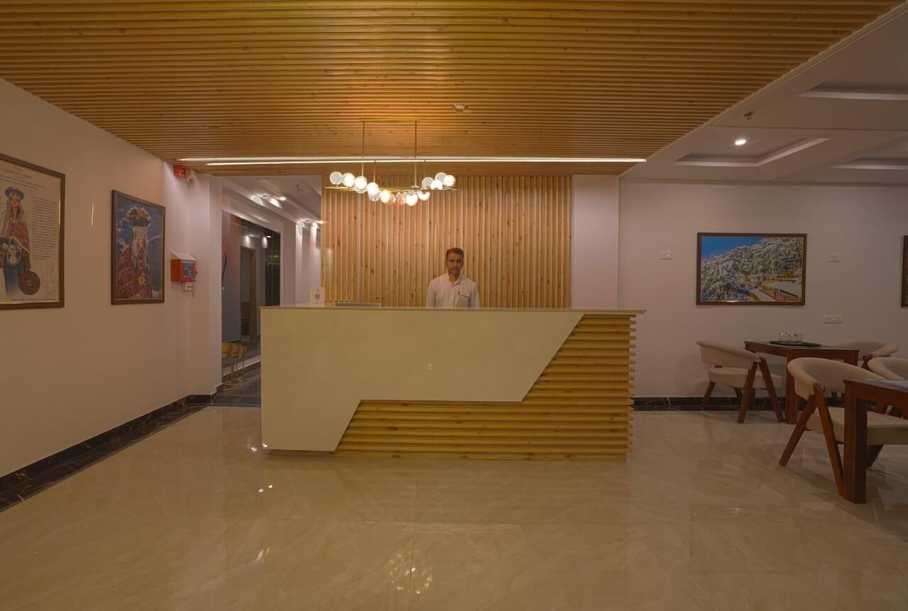 A hotel reception area with a wooden reception desk, a modern chandelier, and framed artwork on the walls.