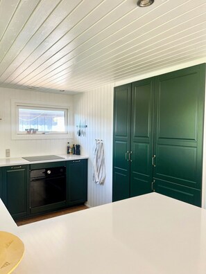 A kitchen with white cabinetry, a black dishwasher, and a window above the sink. - Charming summer house on a secluded plot (Glesborg)