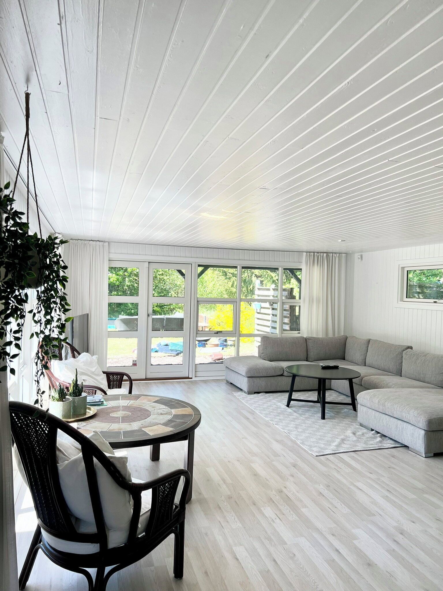 A modern living room with a wooden ceiling, a grey sectional sofa, a round coffee table, and a dining area with a table and chairs.