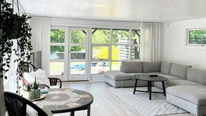 A modern living room with a wooden ceiling, a grey sectional sofa, a round coffee table, and a dining area with a table and chairs.