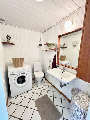 A compact bathroom with a washing machine, toilet, sink, and a mirror above the sink. - Charming summer house on a secluded plot (Glesborg)