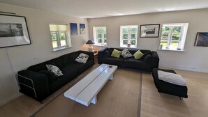 A modern living room with a sectional sofa, a white bench, and a small table. There are multiple windows providing natural light. - Cozy country estate in Vesterborg. (Vesterborg)