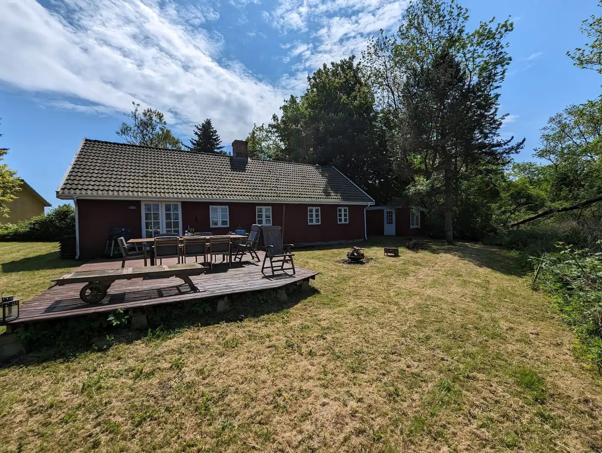 A red house with a tiled roof, a deck with outdoor furniture, and a grassy yard.
