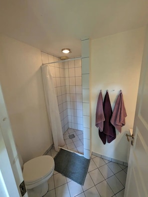 Ein kleines Badezimmer mit Toilette, einer Dusche mit weißem Vorhang und einem Handtuchhalter mit drei Handtüchern.