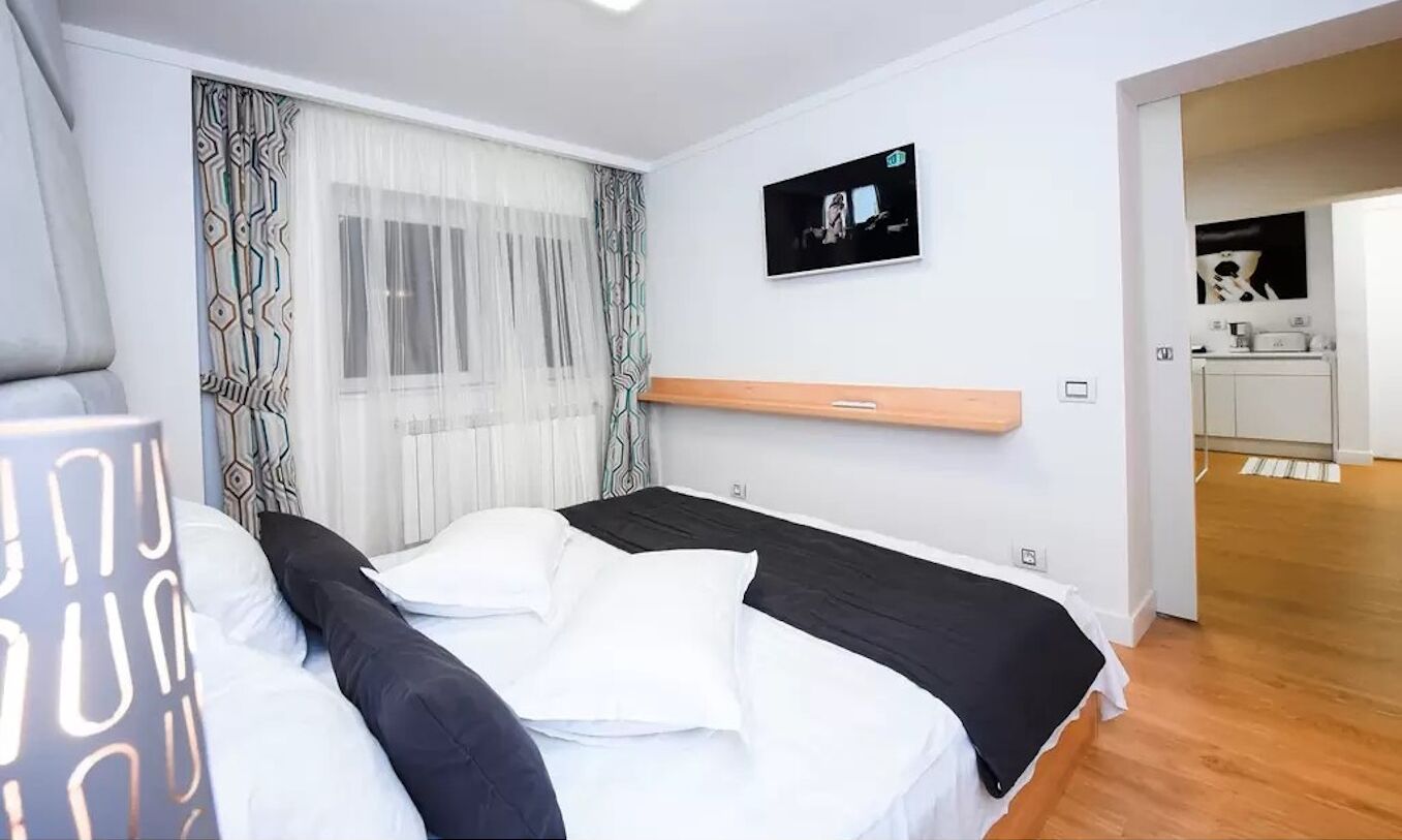 Un dormitori modern amb un llit, un televisor fixat a la paret i vista a la zona de cuina.