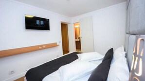 Ett hotellrum med en säng, en tv som är monterad på väggen och en hylla i trä.