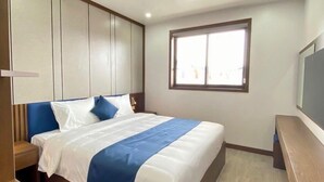 Un dormitorio moderno con una cama grande, cabecera de madera, una mesita de noche, un escritorio y una ventana que proporciona luz natural.