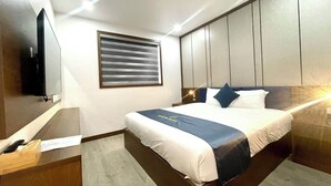 Habitación de hotel moderna con una cama grande, un escritorio con ordenador, televisión y ventana con persianas.