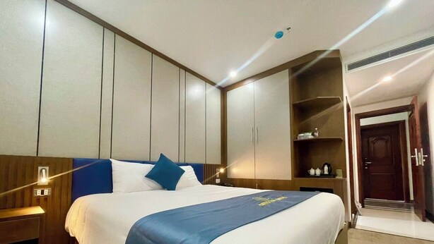 Habitación de hotel con una cama grande, un armario, una mesita de noche y un estante empotrado con objetos.