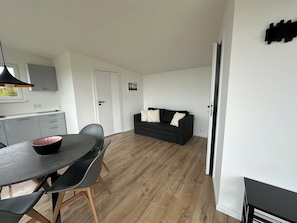 A modern kitchen with a dining area, a black sofa, and a wooden floor.
