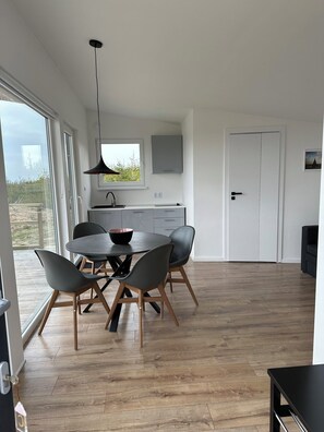 A modern kitchen with a dining area, large windows, and a view of the outdoors.