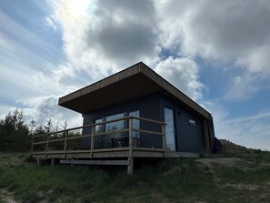 Une cabane moderne dotée d’une terrasse en bois, de grandes fenêtres et d’un toit à pente.