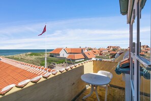 A balcony with a view of a coastal town, a flag, and a table.