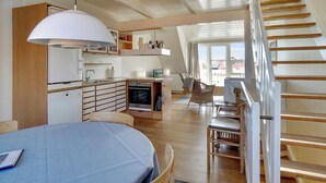 Une cuisine moderne dotée d’un four encastré, un coin repas avec une table et des chaises, et un escalier menant à un niveau supérieur.