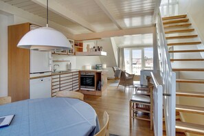 A modern kitchen with a built-in oven, a dining area with a table and chairs, and a staircase leading to an upper level.