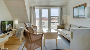 Un salon moderne comprenant une télévision, un canapé, des fauteuils et un balcon offrant une vue sur les immeubles.