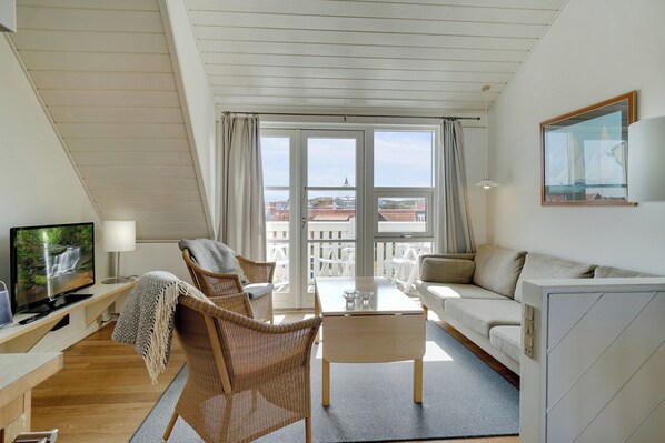 A modern living room with a television, sofa, chairs, and a balcony with a view of buildings.
