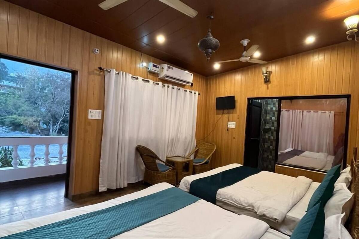 A hotel room with two beds, a ceiling fan, an air conditioning unit, and a view of the outdoors.