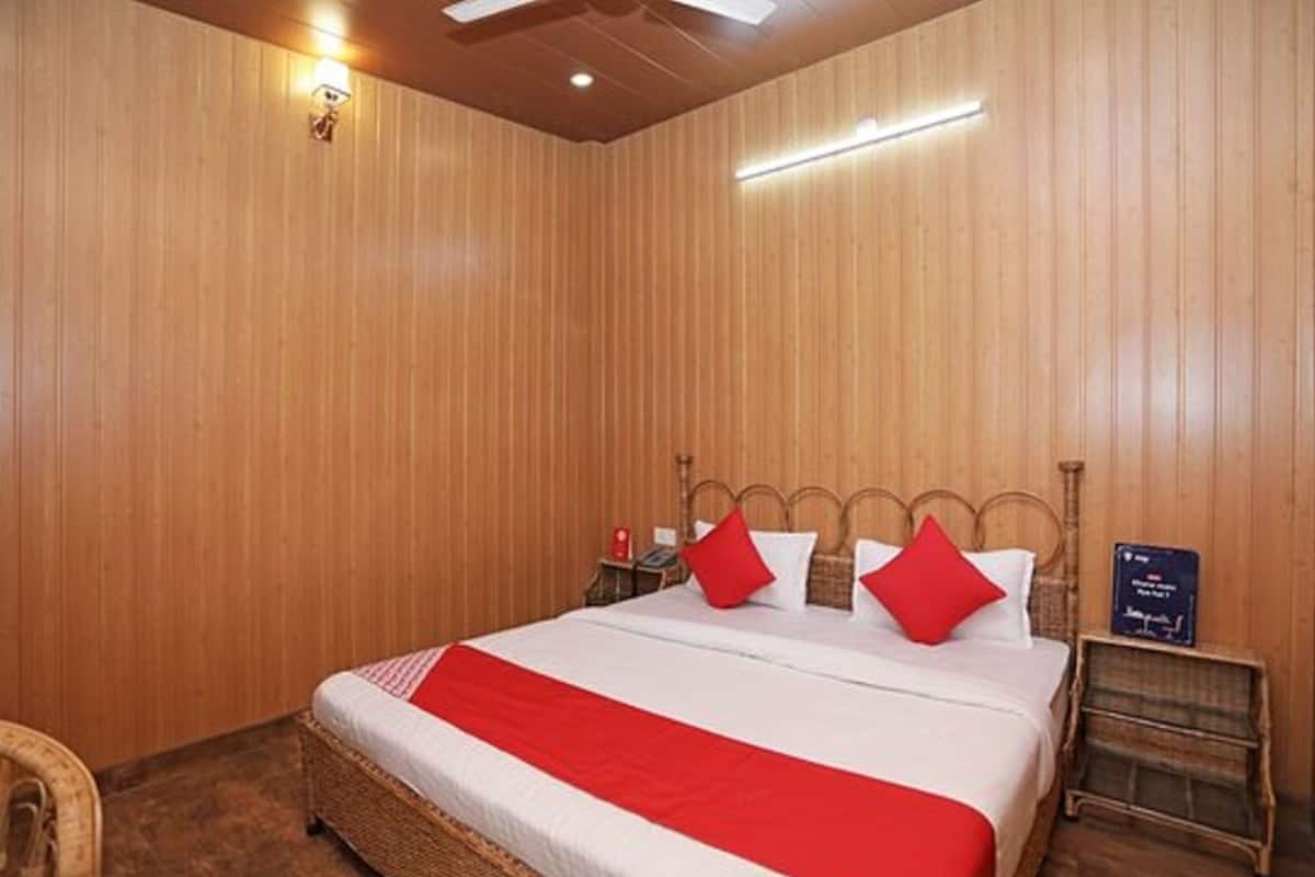 A wooden-paneled room with a bed, red pillows, a nightstand, and a small table.