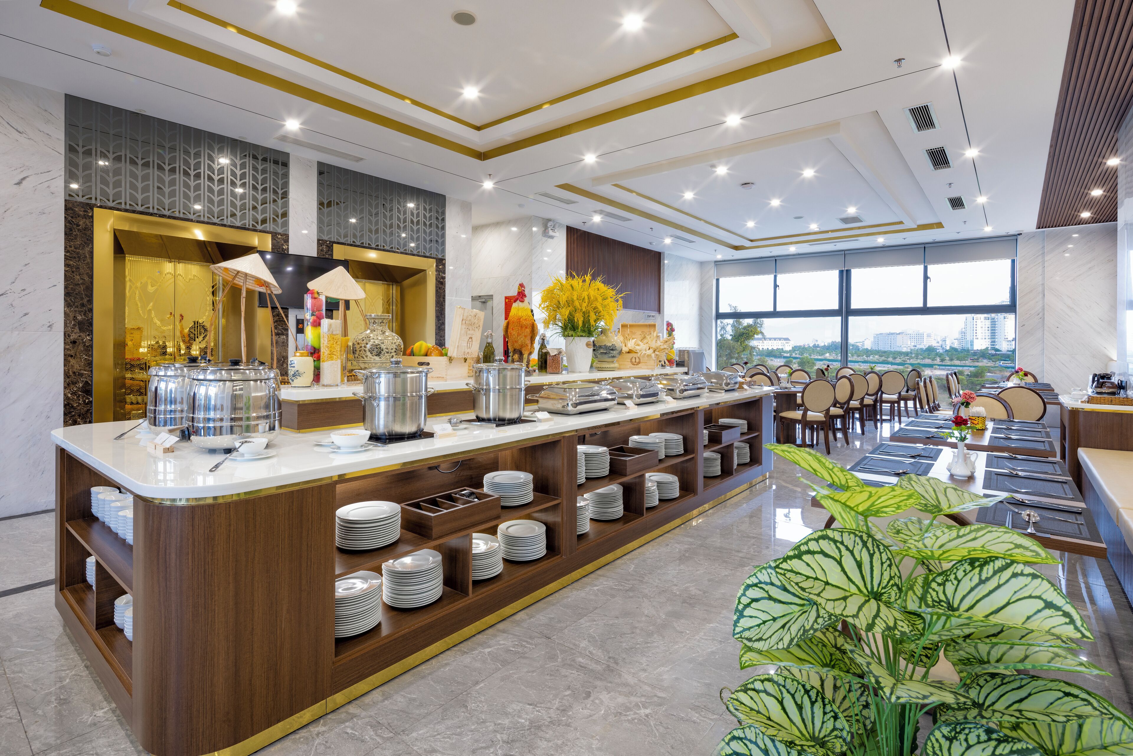 Un hall d’hôtel moderne doté d’un buffet central, de différents espaces aménagés pour s’asseoir et d’une grande fenêtre offrant une vue sur la ville.