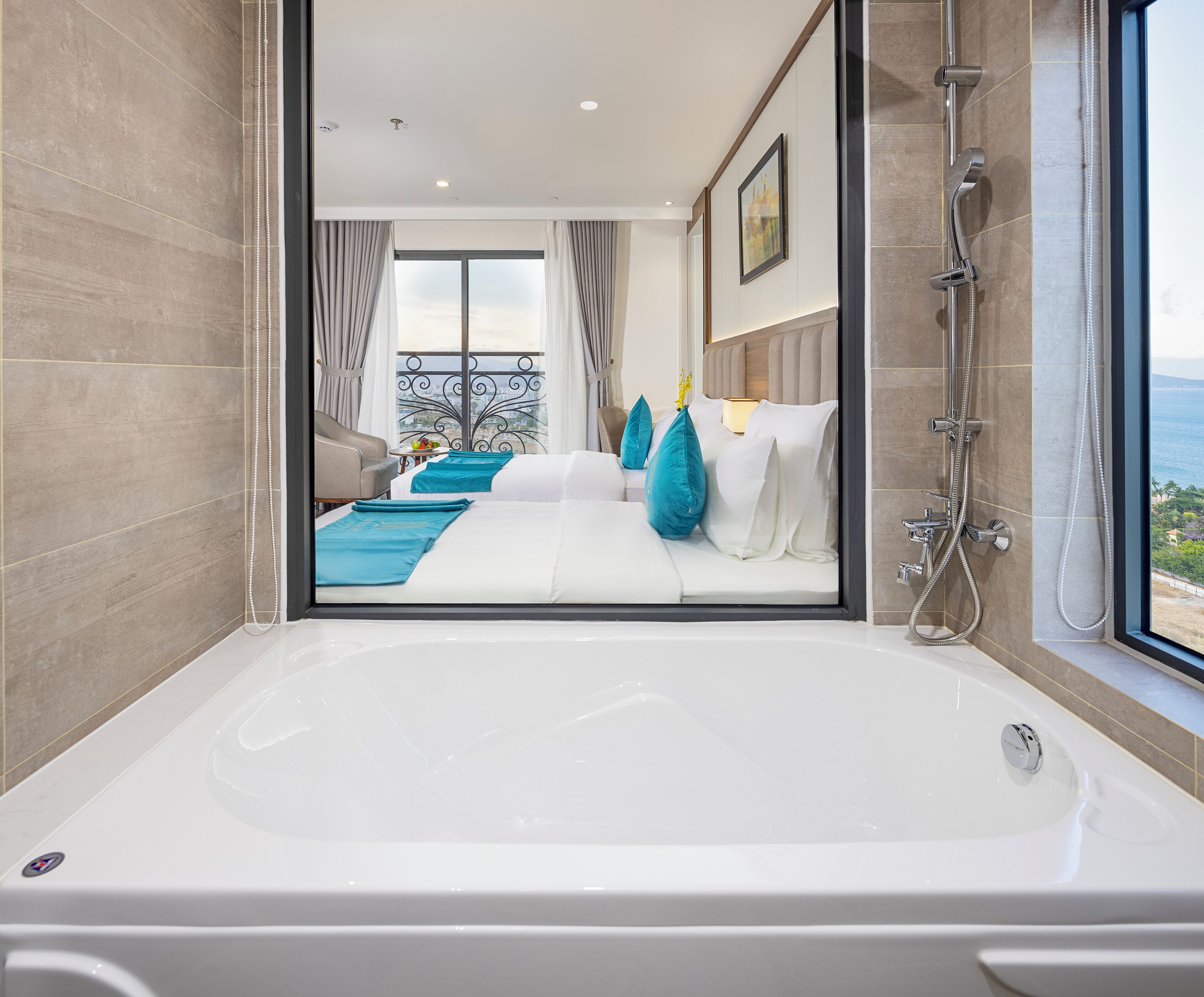 A modern hotel room with a large bathtub, a balcony with a view, and a neatly arranged bed with blue and white bedding.