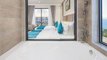 A modern hotel room with a large bathtub, a balcony with a view, and a neatly arranged bed with blue and white bedding.