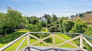 A wooden deck with a railing, a grassy yard, and houses in the background.